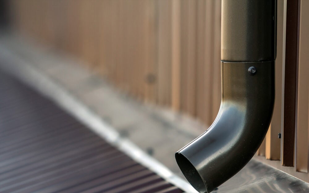 Gutter cleaning in Roseville — dark metal downpipe outlet beside a corrugated roof gutter