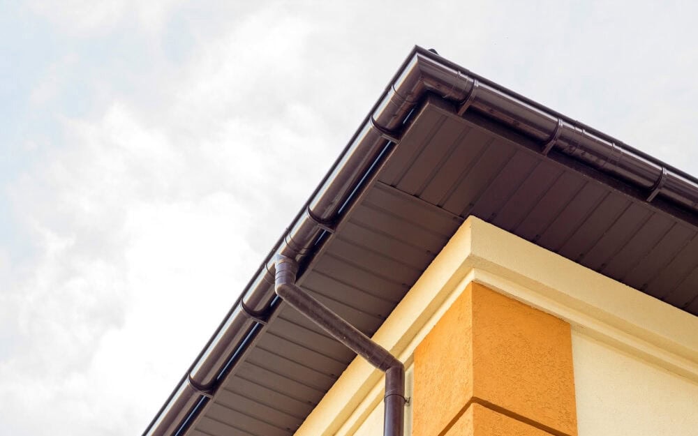 Gutter cleaning in Wahroonga — brown gutter and downpipe on the corner eave of a rendered house